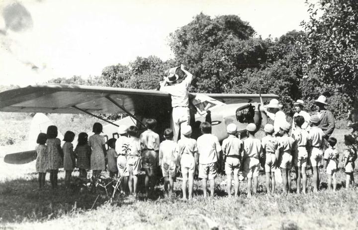 Children gathered in front of a small mission aeroplane