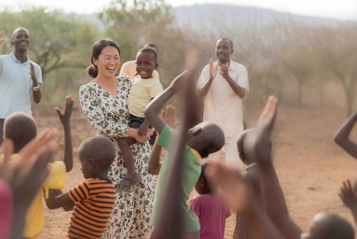 A woman holding a child among children raising their hands